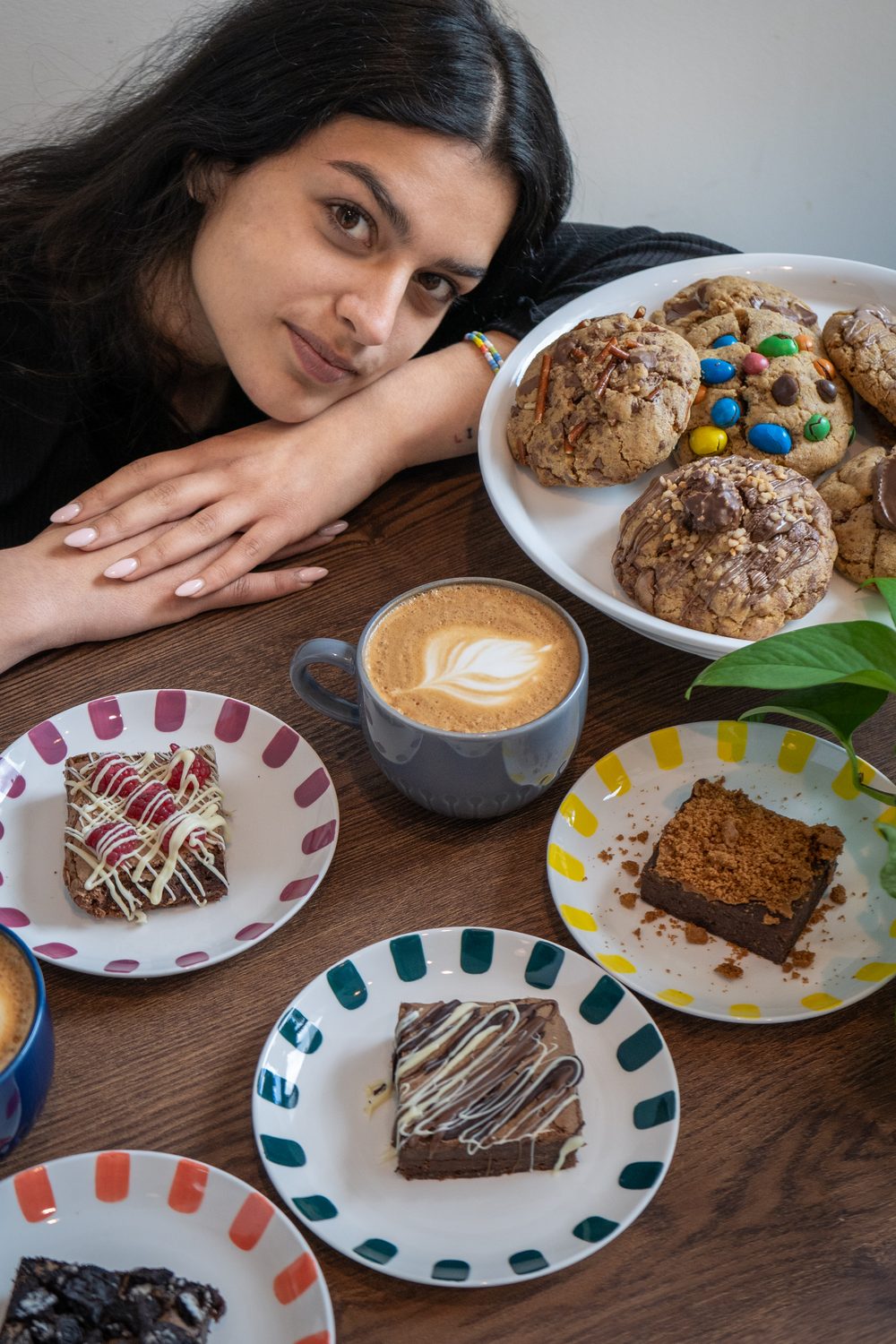 Young woman resting her head on her hands at a café table with cookies, brownies and a latte